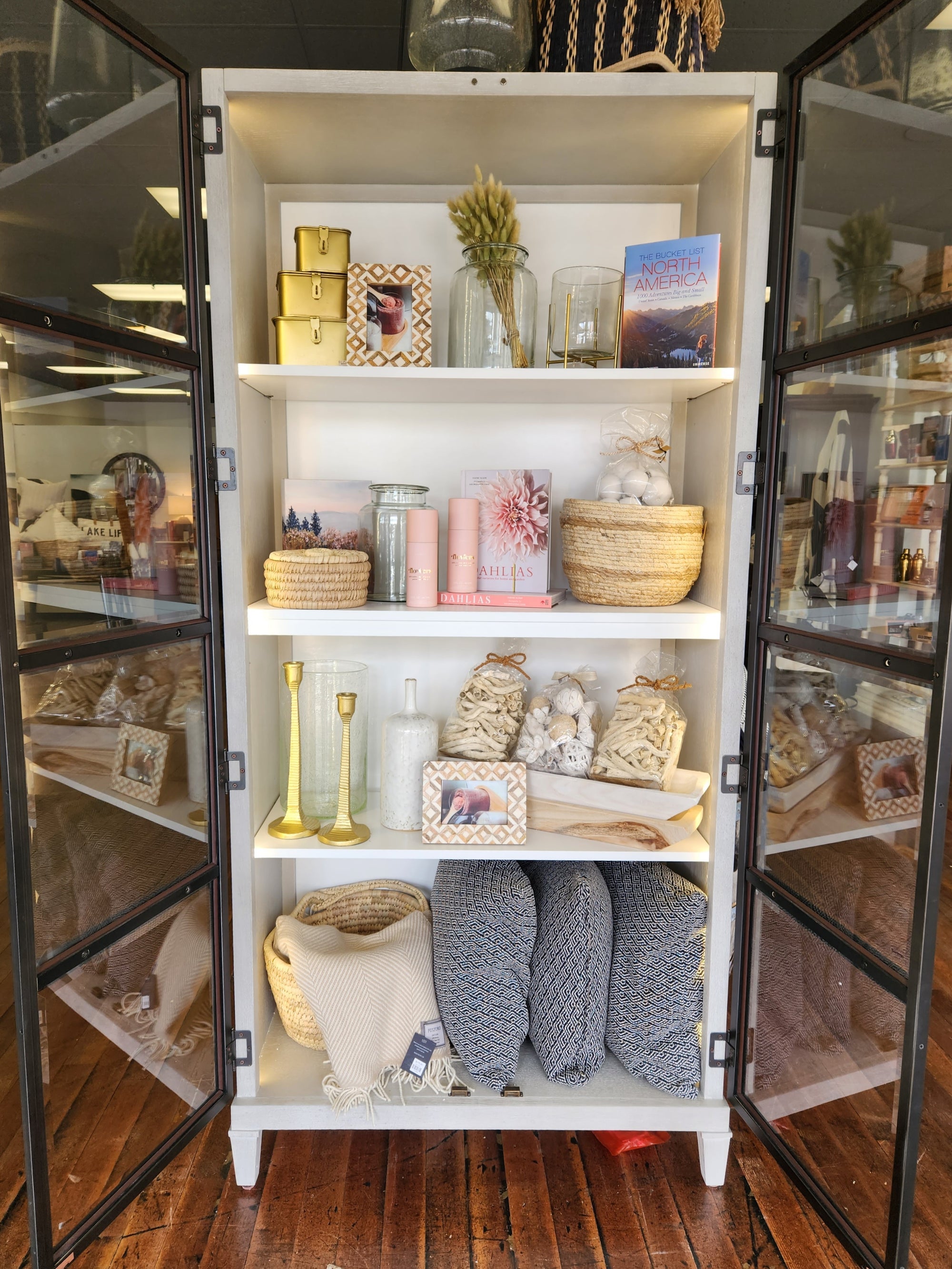 Lighted display case with gold accents, pillows and blankets, and natural baskets