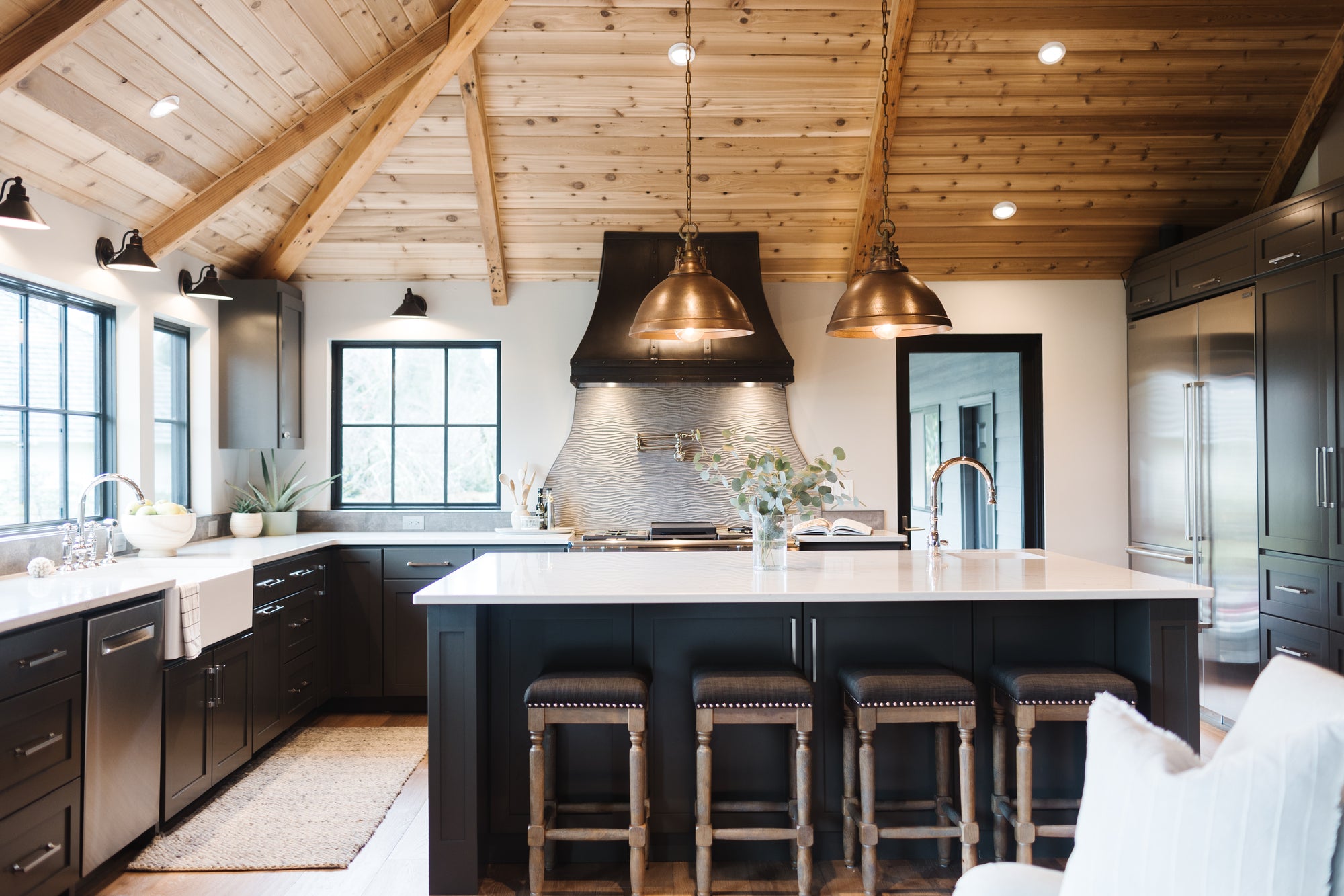 Bright kitchen design with black cabinets, white walls and counters, and gold pendants