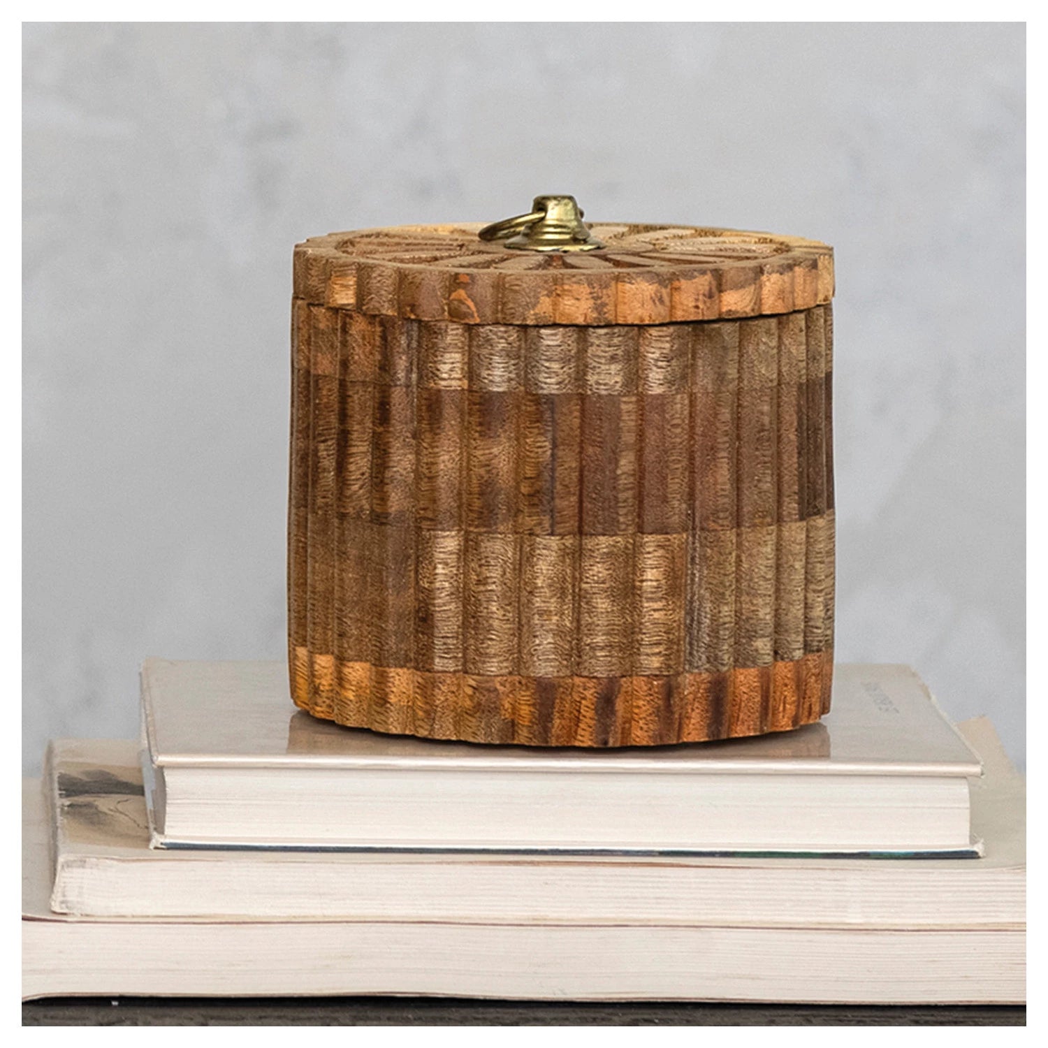 Hand carved mango wood pleated box with matching lid and metal pull resting on top two books. 