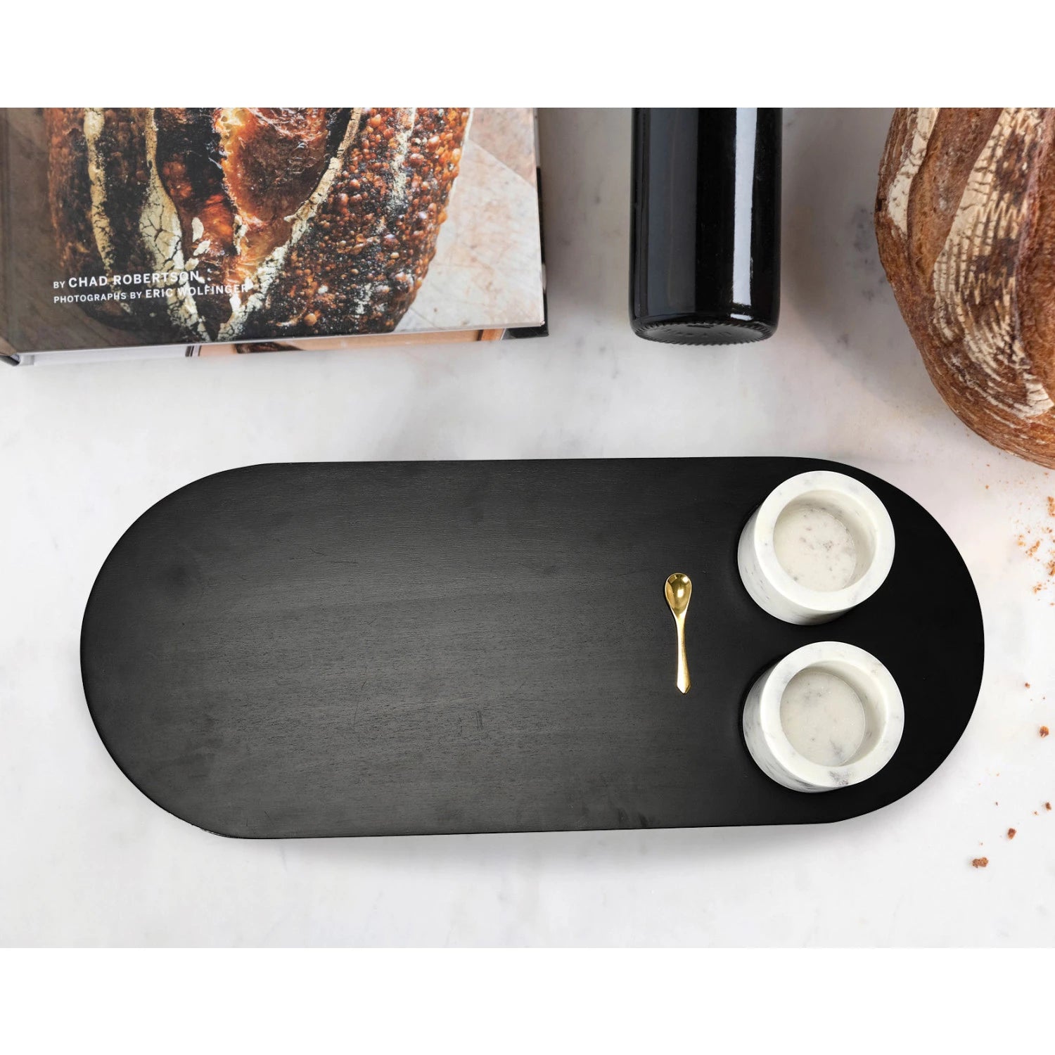 Overhead look at an oval black wood tray with two marble bowls inset into the tray and a little gold spoon.
