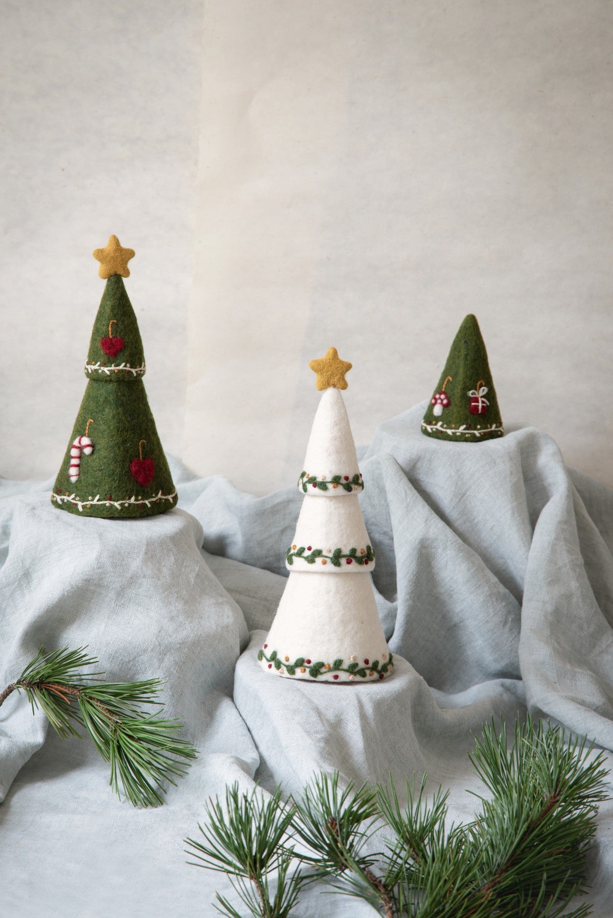 Three decorative Christmas trees on a light gray surface with a plain background