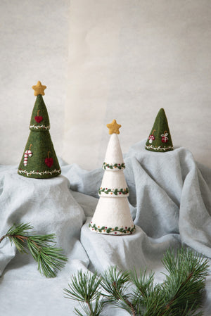 Three decorative Christmas trees on a light gray surface with a plain background