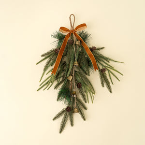 Decorative wall hanging with greenery, pinecones, and a rust brown velvet bow ribbon on a beige background