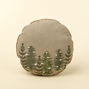 Round holiday pillow with embroidered snowy Alpine trees on a beige background. 