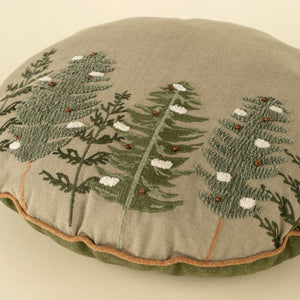 Round pillow with embroidered green tree foliage designs on a beige background. 