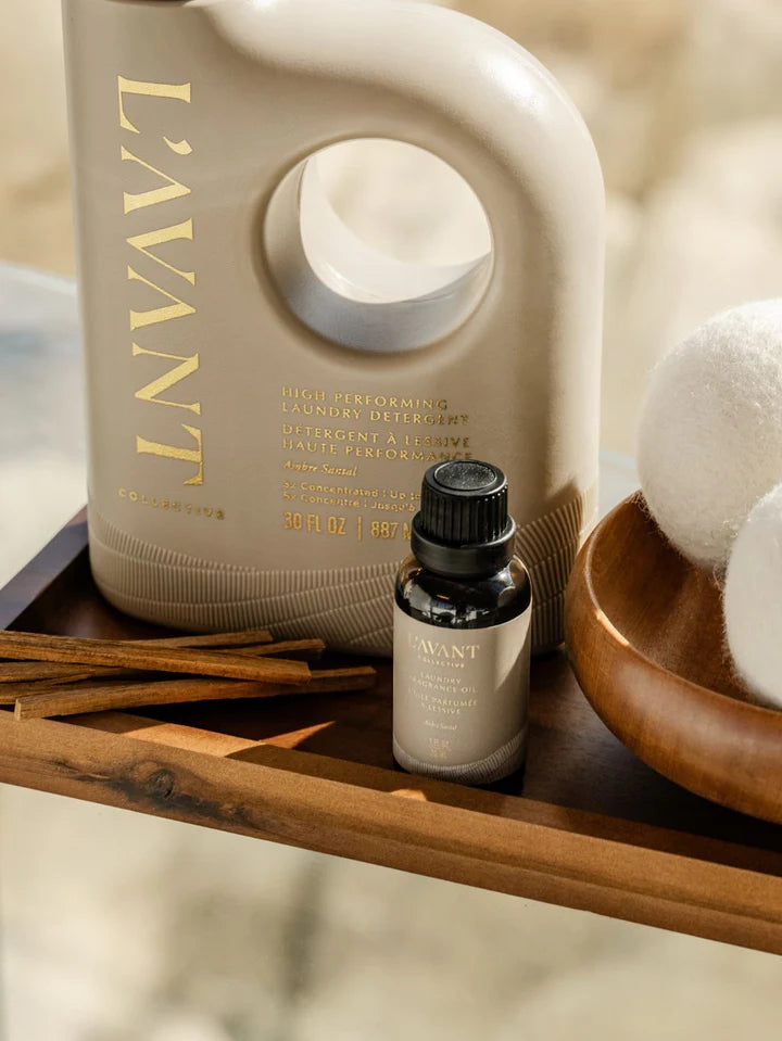 L'AVANT laundry detergent bottle and essential oil bottle on a wooden surface with decorative items.