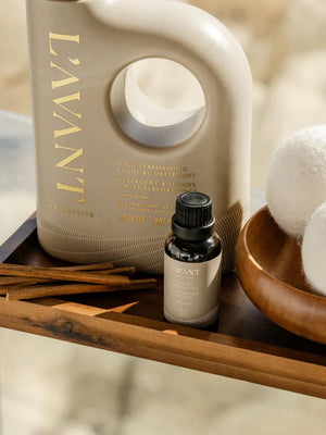 L'AVANT laundry detergent bottle and essential oil bottle on a wooden surface with decorative items.