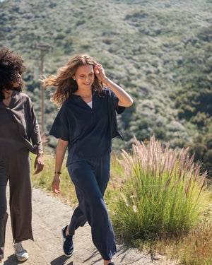 Two people walking on a trail with a scenic background of hills and greenery. Model wearing navy cotton tee shirt and matching pants. 