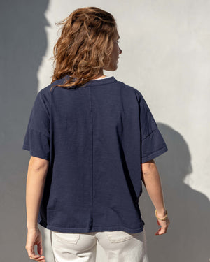 Person wearing a navy blue cotton tee shirt against a gray wall. Back view. 