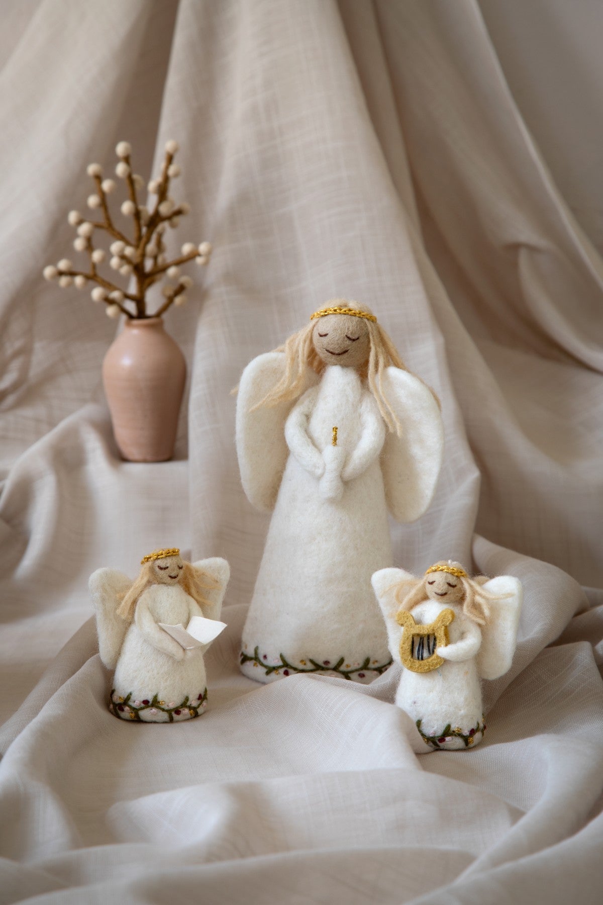 Three wool angel figurines on a soft fabric background