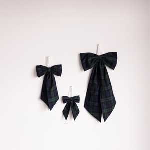 Collection of three blue and green plaid holiday hanging bows in small, medium, and large hanging against a white background. 