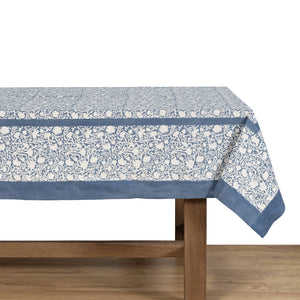 Tablecloth with floral pattern and blue border on a wooden table. Couleur Nature Meadows Bleu. 