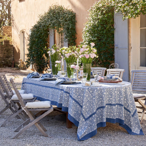 Outdoor table setting with a floral tablecloth and chairs in a garden.