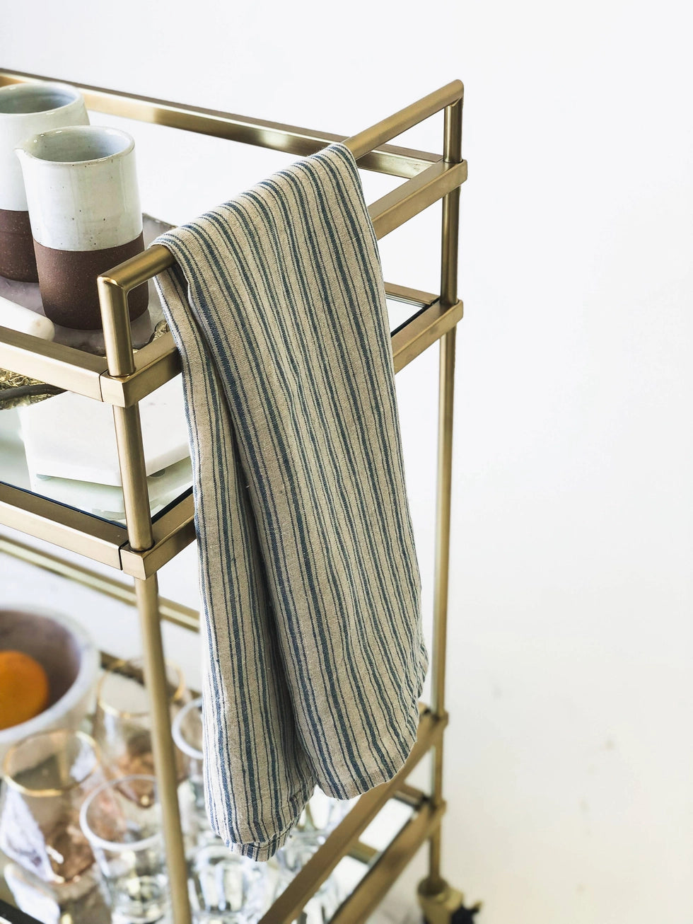 Gold bar cart with a striped blue towel draped over side, on a white background