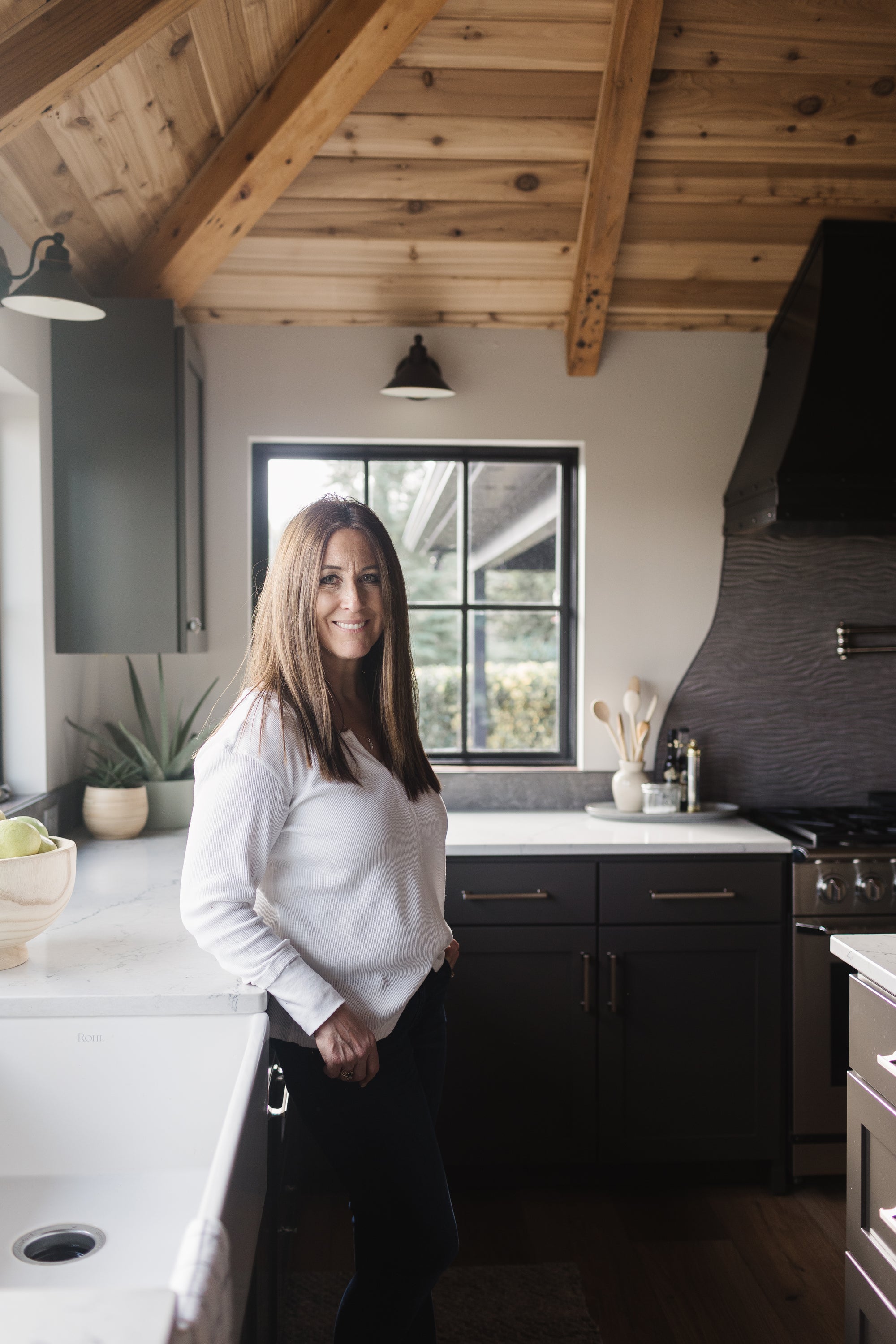 Owner Juleen Pudists standing in a white kitchen with black accents and a steel range hood.