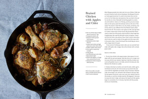 Braised chicken with apples and cider in a skillet on a blue surface, next to text.