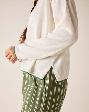 Person wearing a white sweater with green trim and green striped pants on a plain background