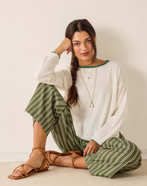 Woman wearing a white sweater and green striped pants sitting on a light-colored floor.
