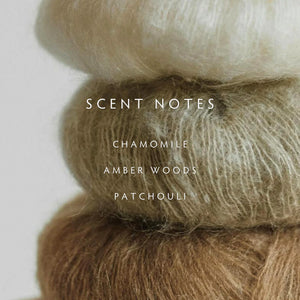 Stack of brown yarn with scented notes- "chamomile, amber woods, and patchouli" text overlay on a light background