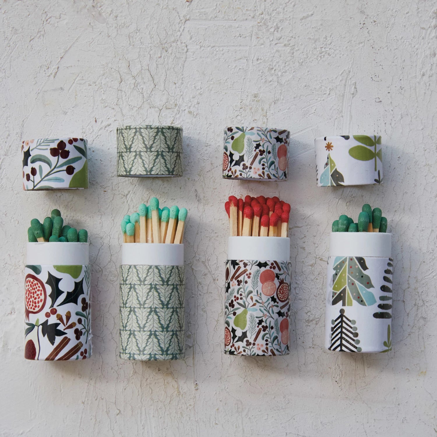 Patterned Christmas tube matchboxes with matches against a textured surface. 