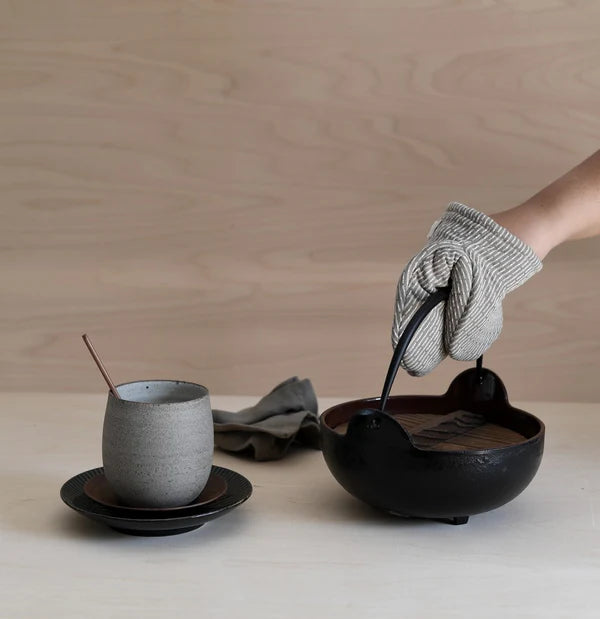 Organic neutral stripe colored mini oven mitt holding cast iron pot. Organic cotton kitchen accessories. 