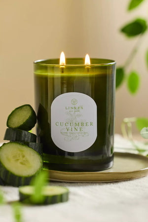 Candle labeled 'Cucumber Vine' with cucumbers stacked on a gold metallic tray against a neutral background. Linnea Botnik collection. 