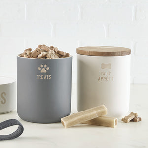 Two pet treat jars with wooden lids on a white surface. 