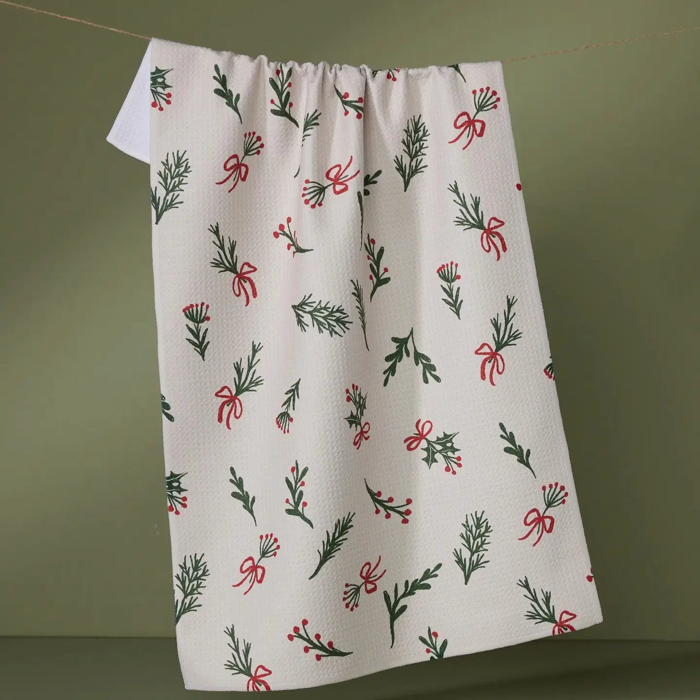 White tea towel with Christmas-themed pattern of bows, holly, and greenery on a plain green background. Geometry. 