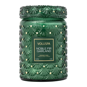 A green glass jar candle with a matching lid, featuring a textured fan pattern and small gold dot accents. The front has a green label with gold text that reads 'VOLUSPA NOBLE FIR GARLAND'.