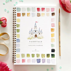 Fairytale watercolor workbook with a castle illustration on a white surface with flowers and a brush. Emily Lex Studios. 