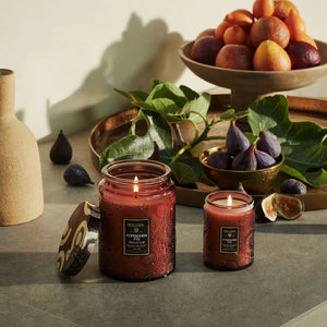 Forbidden Fig candles displayed on a table with assorted fruits including figs, nectarines, and oranges. 
