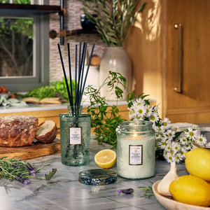 French Cade Lavender candles and diffusers on a kitchen counter with lemons, daisies, and lavender. Voluspa. 