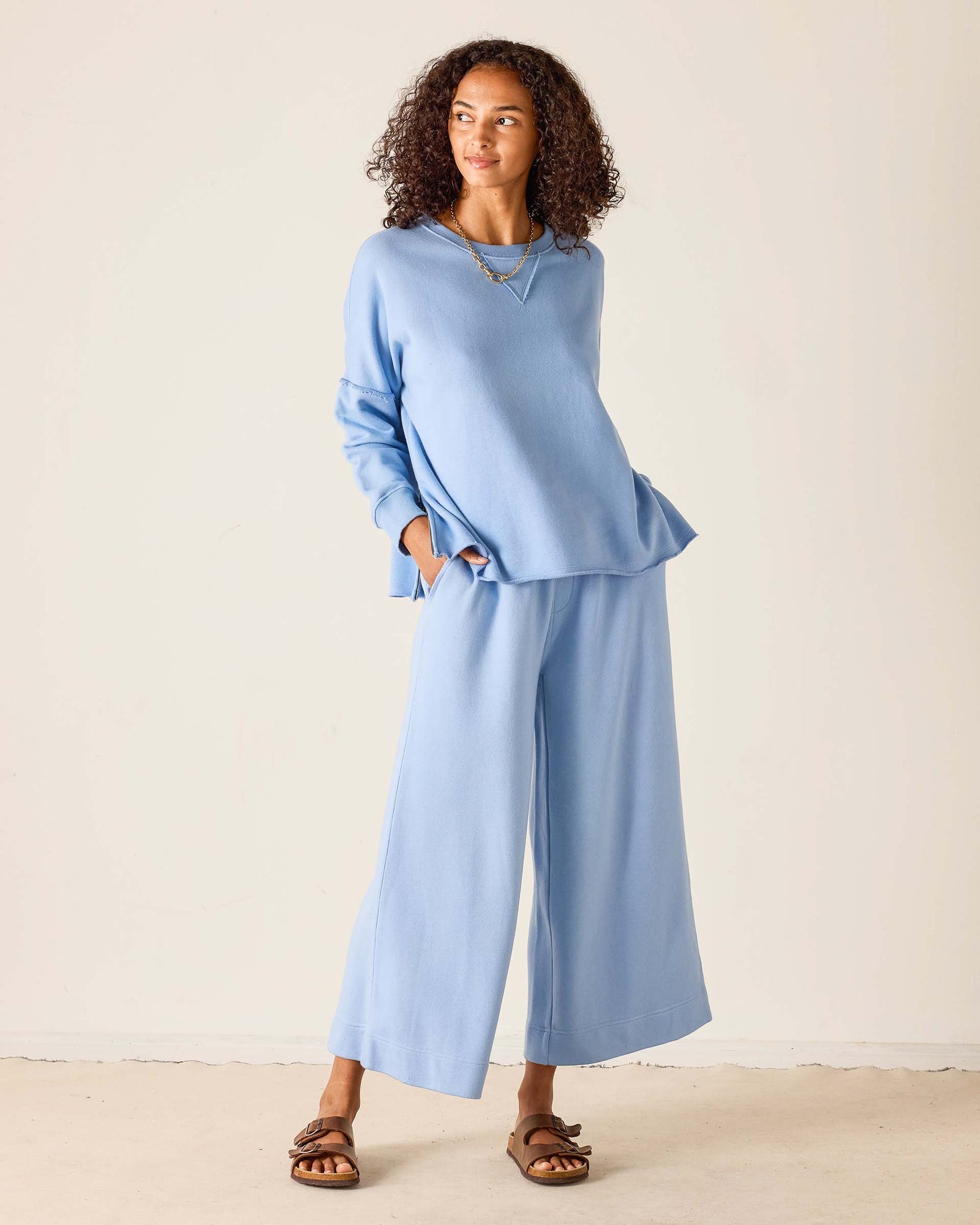 Woman wearing a light blue outfit with wide-leg pants against a plain background