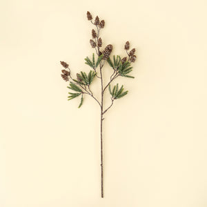 A single artificial pine branch with green needles, brown pinecones, and a long stem, centered on a solid cream background.