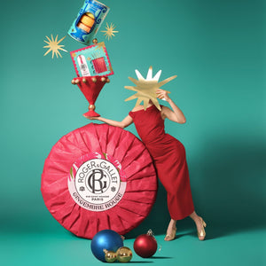 Person in a red dress with a large Roger & Gallet gingerbread red roundel on a teal background. Gingembre Rouge. 