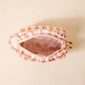 A top-down view of a small fabric pouch with a peach and white gingham check pattern, ruffled trim, and a floral-patterned pink interior, set against a solid beige background.