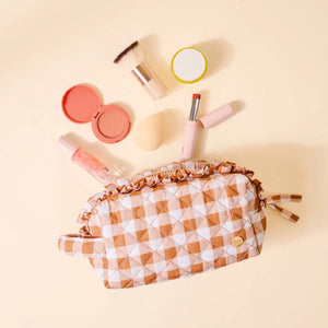 Brown ruffle checkered makeup bag with assorted makeup items on a beige background.