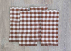 Set of four brown and white checkered linen cloth picnic napkins on a wooden surface. 