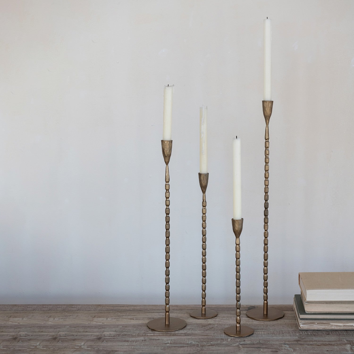 four brass cast iron candle holders in extra large, large, medium, and small sizes with candles in them. 