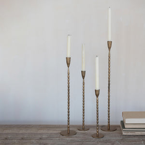 four brass cast iron candle holders in extra large, large, medium, and small sizes with candles in them. 