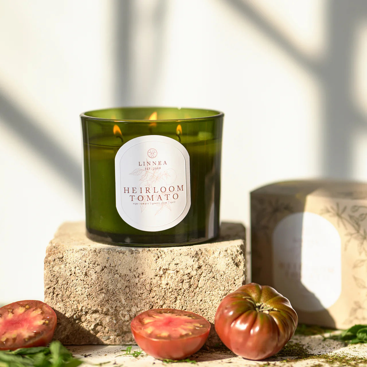 Linnea Heirloom Tomato three wick candle on a terracotta stone surface surrounded by tomatoes.