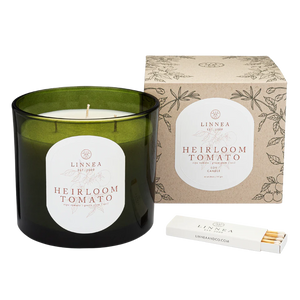 Twenty-six ounce moss green candle labeled 'Heirloom Tomato' by Linnea with packaging and matches on a white background