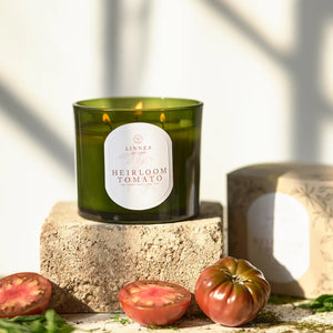 Linnea Heirloom Tomato three wick candle on a terracotta stone surface surrounded by tomatoes.
