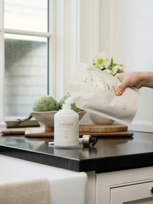 L'AVANT high performing hand lotion refill pouch being poured into a L'AVANT white glass bottle. 
