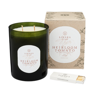 Green candle labeled 'Heirloom Tomato' by Linnea with packaging and matches on a white background