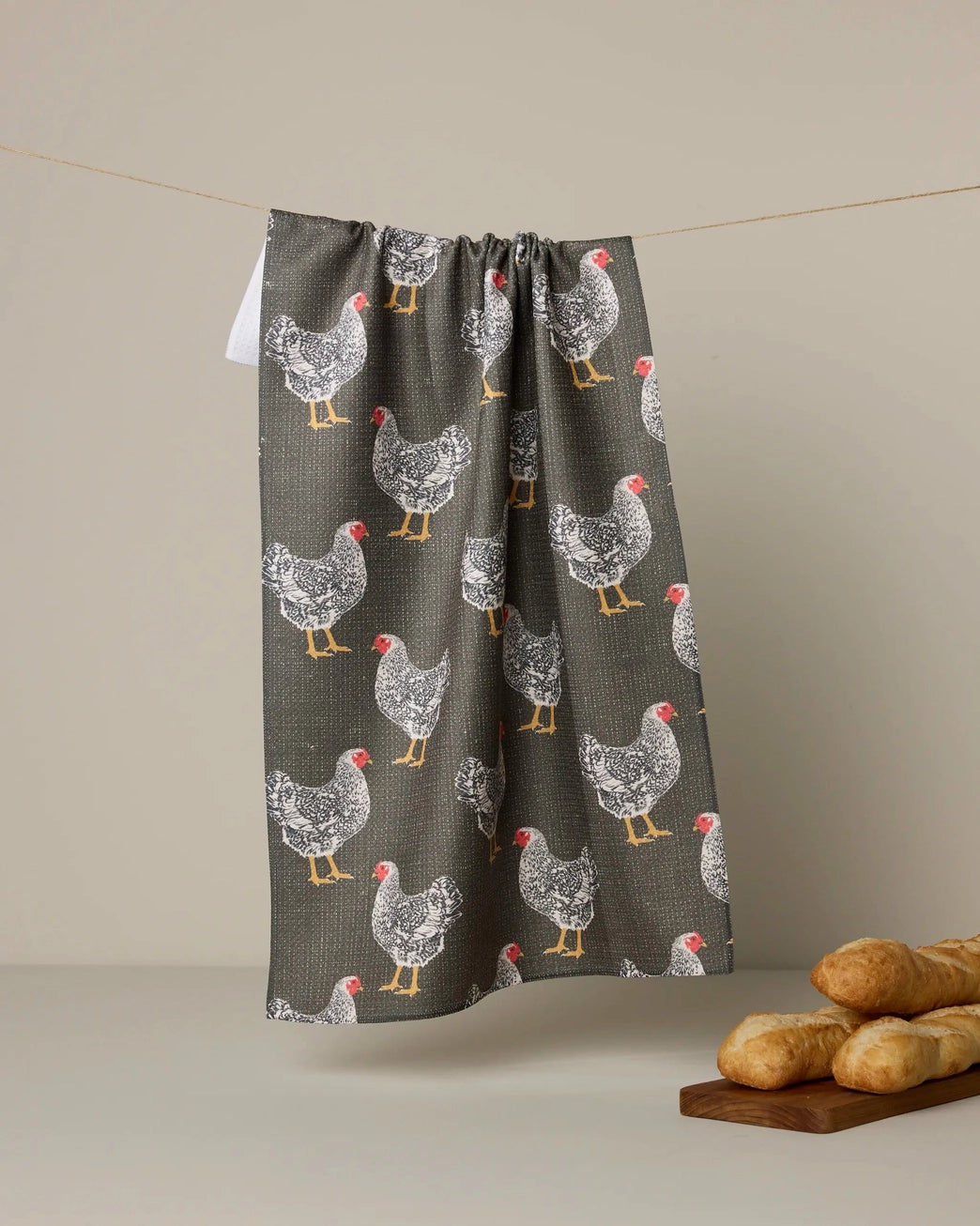 Dark grey kitchen and bathroom towel with hen pattern hanging on clothes wire; loaves of bread on serving tray laying on floor. Geometry House. 