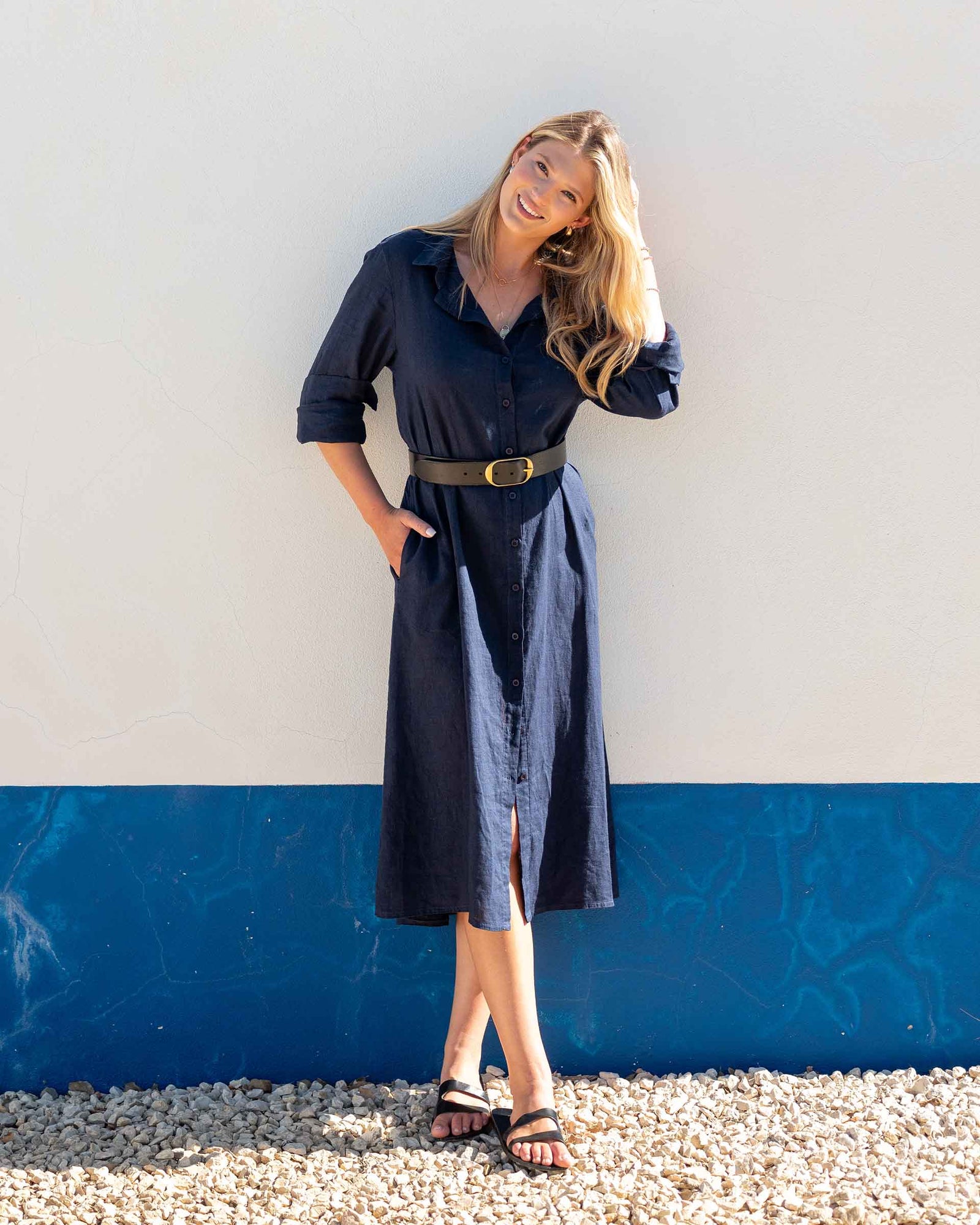 Woman wearing a navy button up linen dress against a white and blue wall.