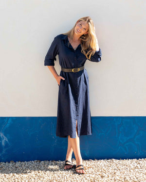 Woman wearing a navy button up linen dress against a white and blue wall.