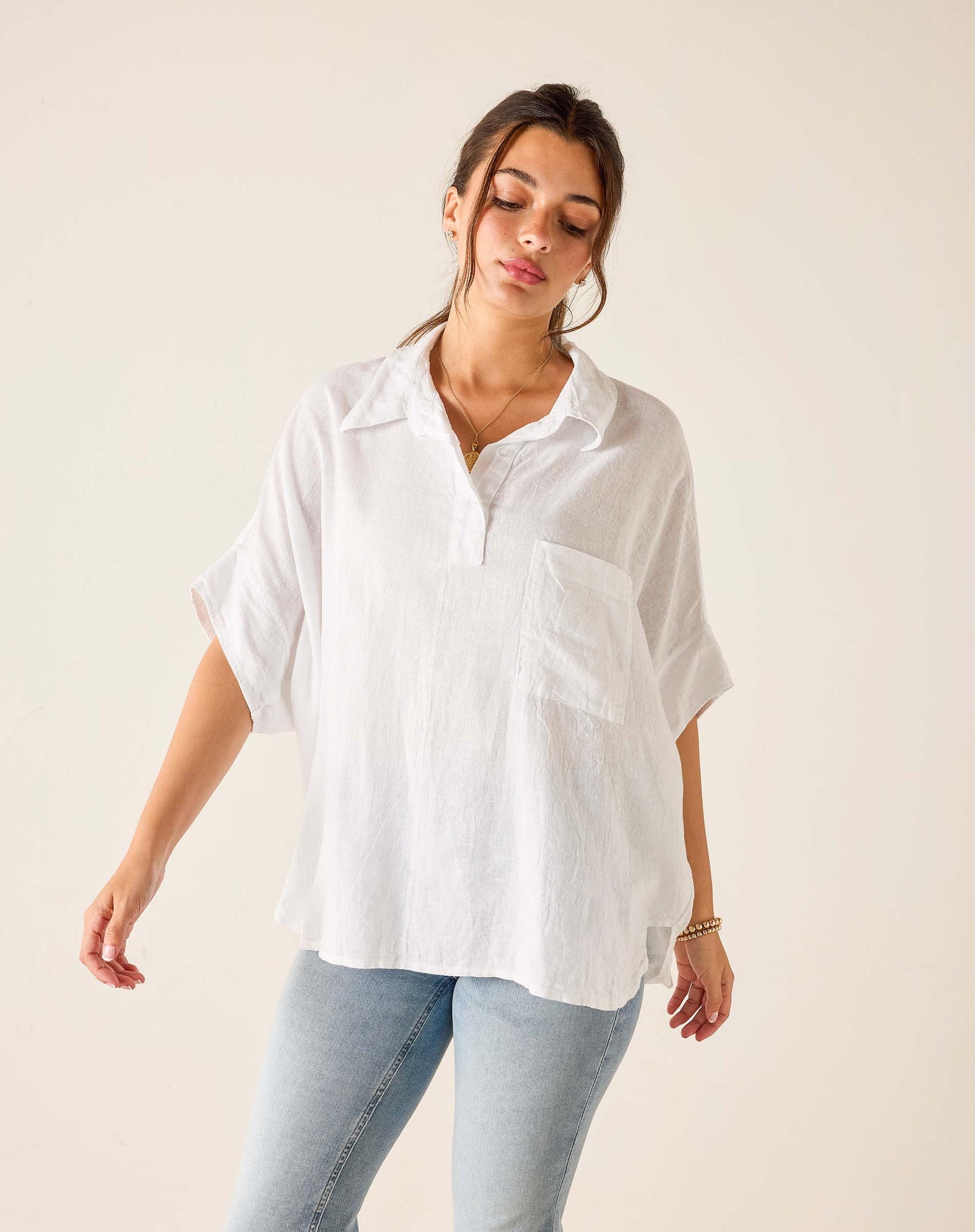 Woman wearing a white oversized shirt and light blue jeans against a plain background. Hermosa collared shirt. 