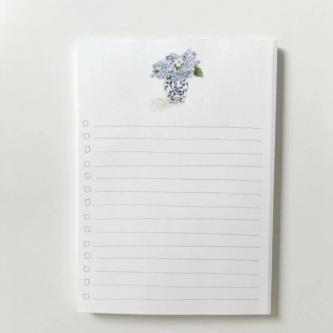 Notepad with lined pages and watercolor illustration of hydrangea bouquet on a white background.